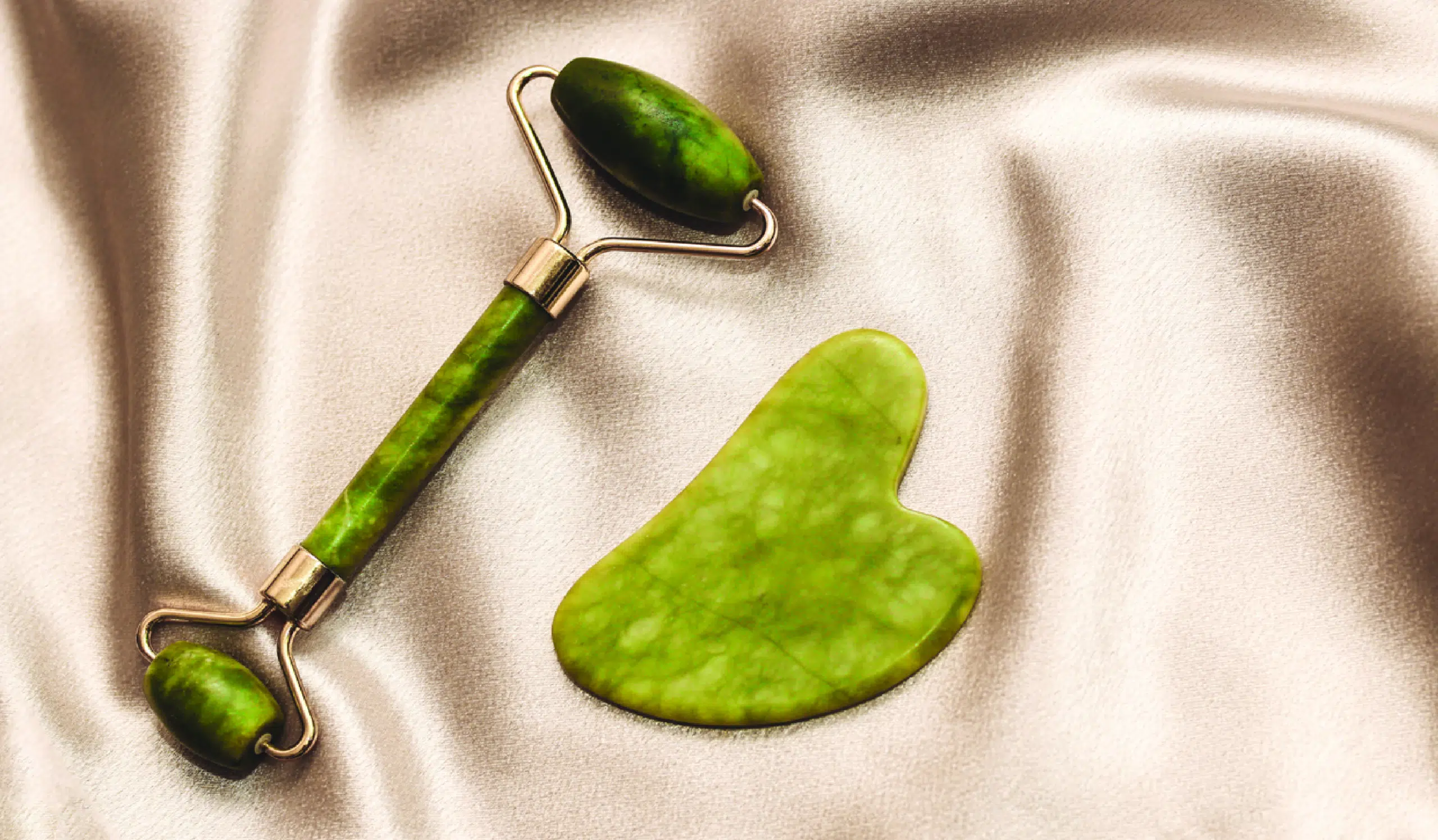 An image showcasing a jade roller and a Gua Sha tool placed on a clean surface. The jade roller has a smooth, cool surface with a handle on one end, while the Gua Sha tool features a curved, flat edge with intricate etchings. Both tools are commonly used in skincare routines for facial massage and lymphatic drainage.